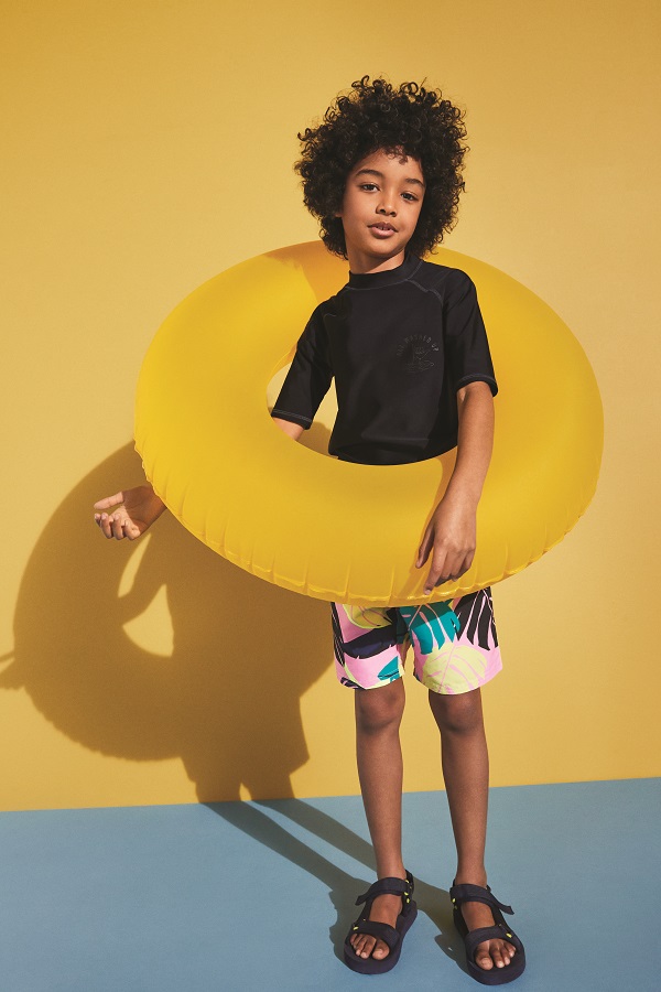 A young boy wearing a black tshirt, swimming shorts and a yellow rubber ring.