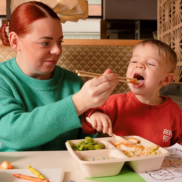 Photo of mum feeding her child sushi with chopsticks